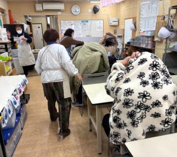 つぎは避難訓練です。地震発生の音が鳴るとともに、机の下にもぐるか、身の安全を確保します。揺れが収まった時点で職員がヘルメットを各ご利用者に手渡します。自力歩行の可能なご利用者から、建物を出て第１避難場所へ避難を開始します。